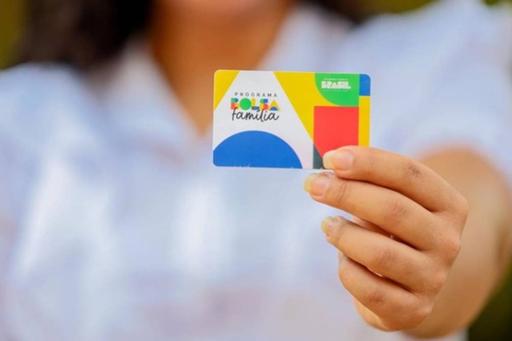 Mão segurando cartão do Bolsa Família com logo colorido do programa.