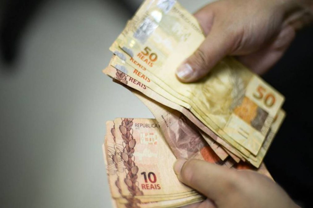 Pessoa conta notas de reais referente ao 13º salário