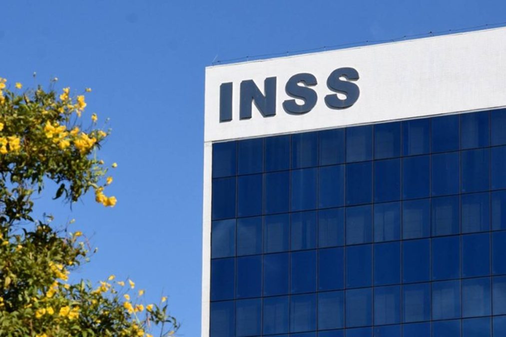 Fachada de prédio do INSS com letreiro e céu azul ao fundo.